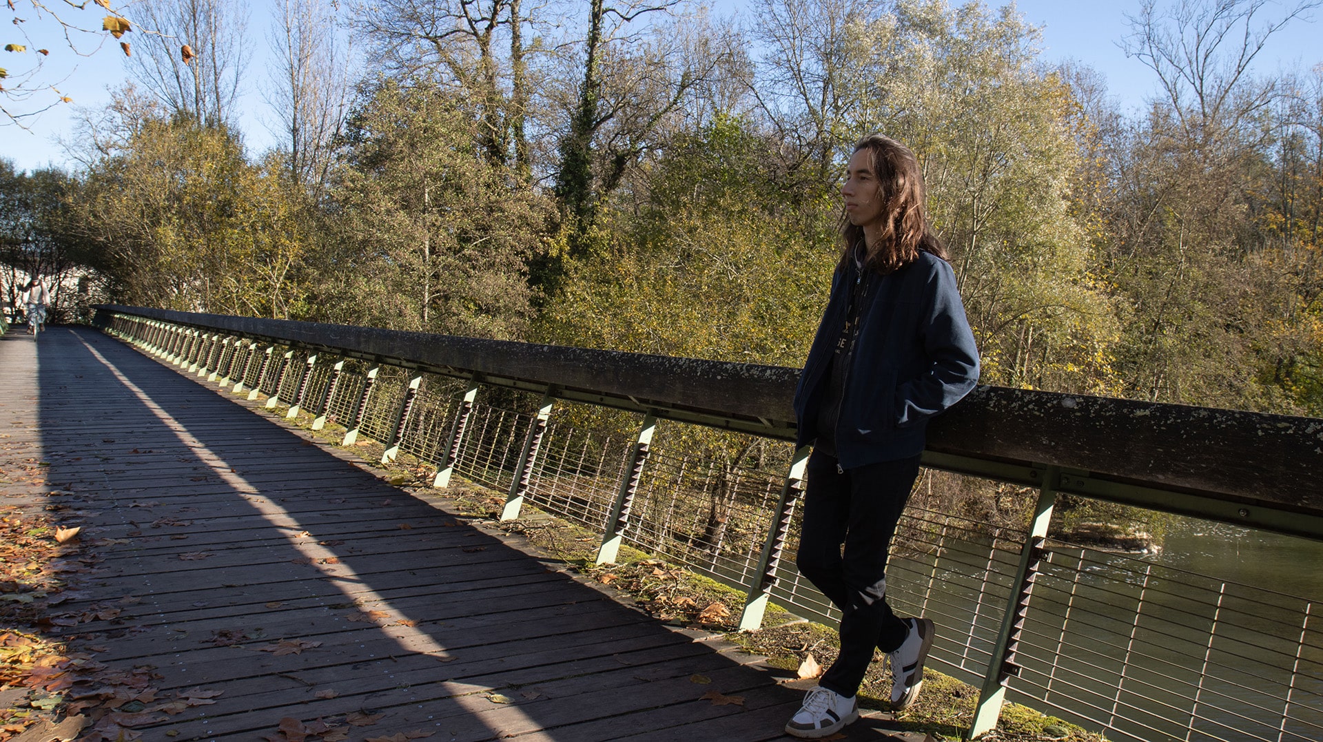 Un jeune étudiant sur un pont devant un fleuve entouré d'arbres, regardant dans le lointain